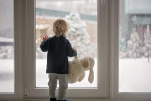 small-child-with-stuffed-animal-looking-out-the-window-at-the-snow